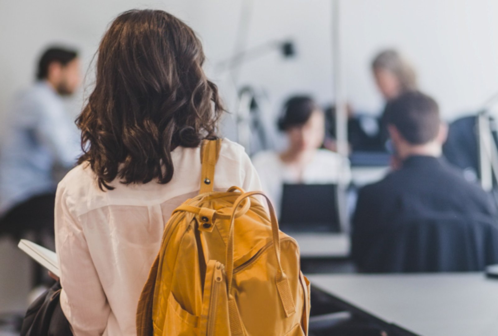 The back view of a girl wearing a yellow backpack going to her class
