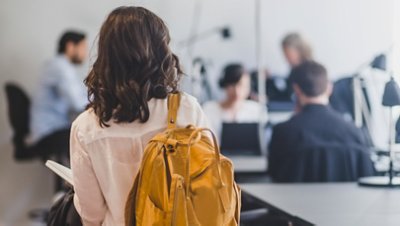 The back view of a girl wearing a yellow backpack going to her class