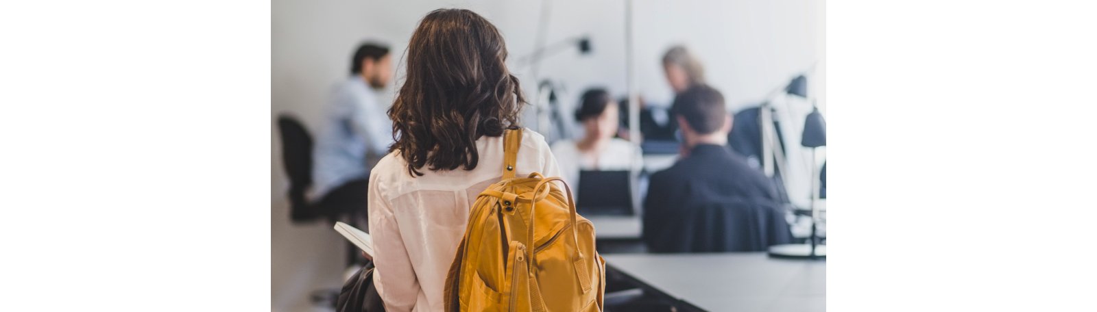 The back view of a girl wearing a yellow backpack going to her class
