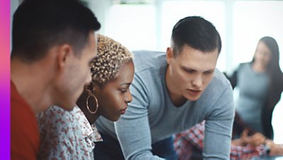 A man showing something to his two colleagues and there is a blurred image of a woman on their far left.