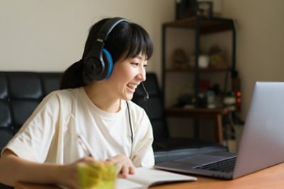 Photo of a Japanese woman online learning at home. She wearing headset and note taking.
