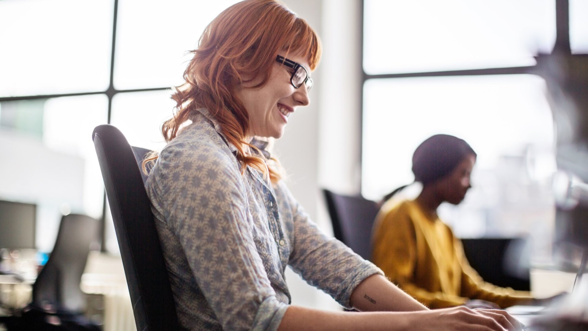 A smiling woman working at her desk in a modern office.