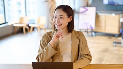 Women smiling on a nude blazer with laptop on her wooden table