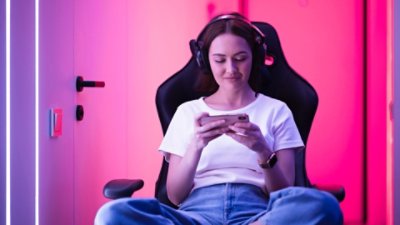 Women sitting on a gaming chair using her phone and wearing headset