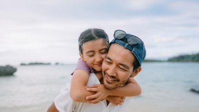 A father carrying his daughter on his back while in the beach