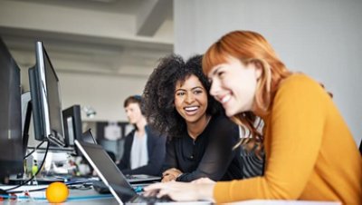 Two young women working together on laptop with male colleague in background