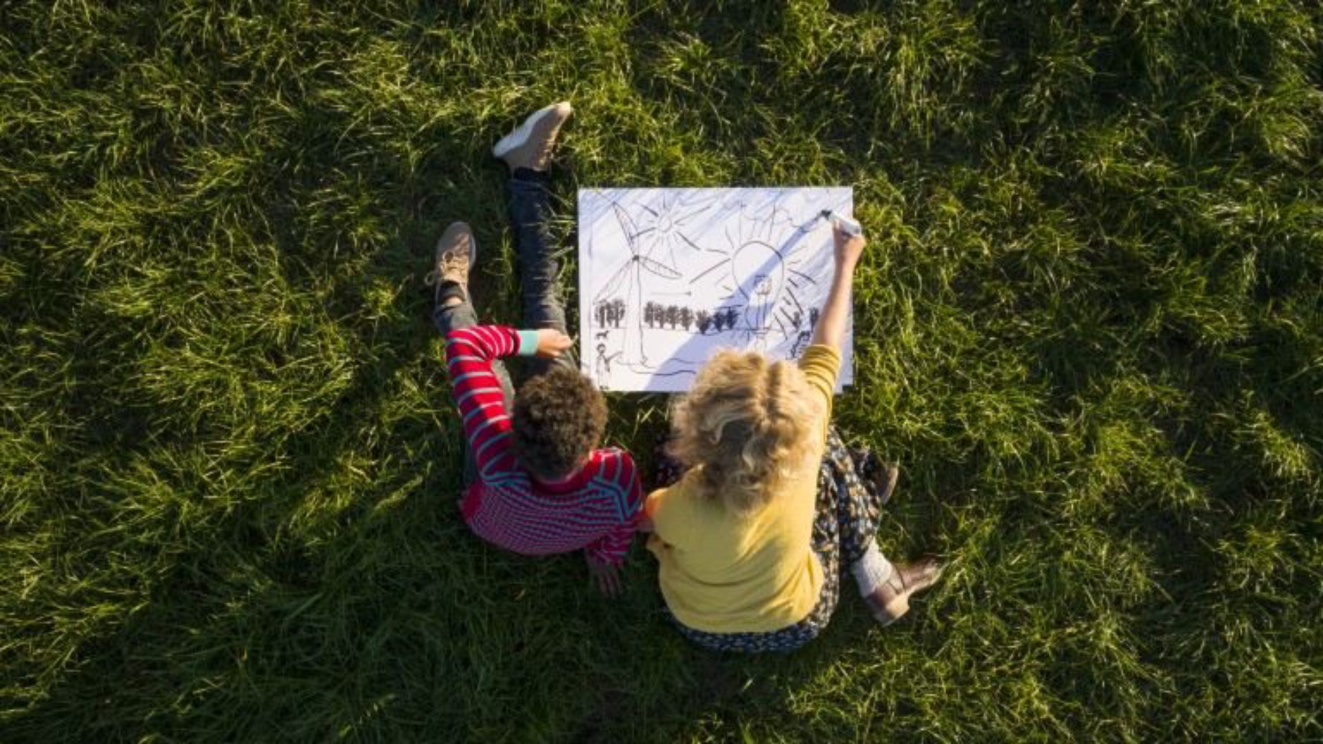 Top view of two kids sitting on a green field and drawing