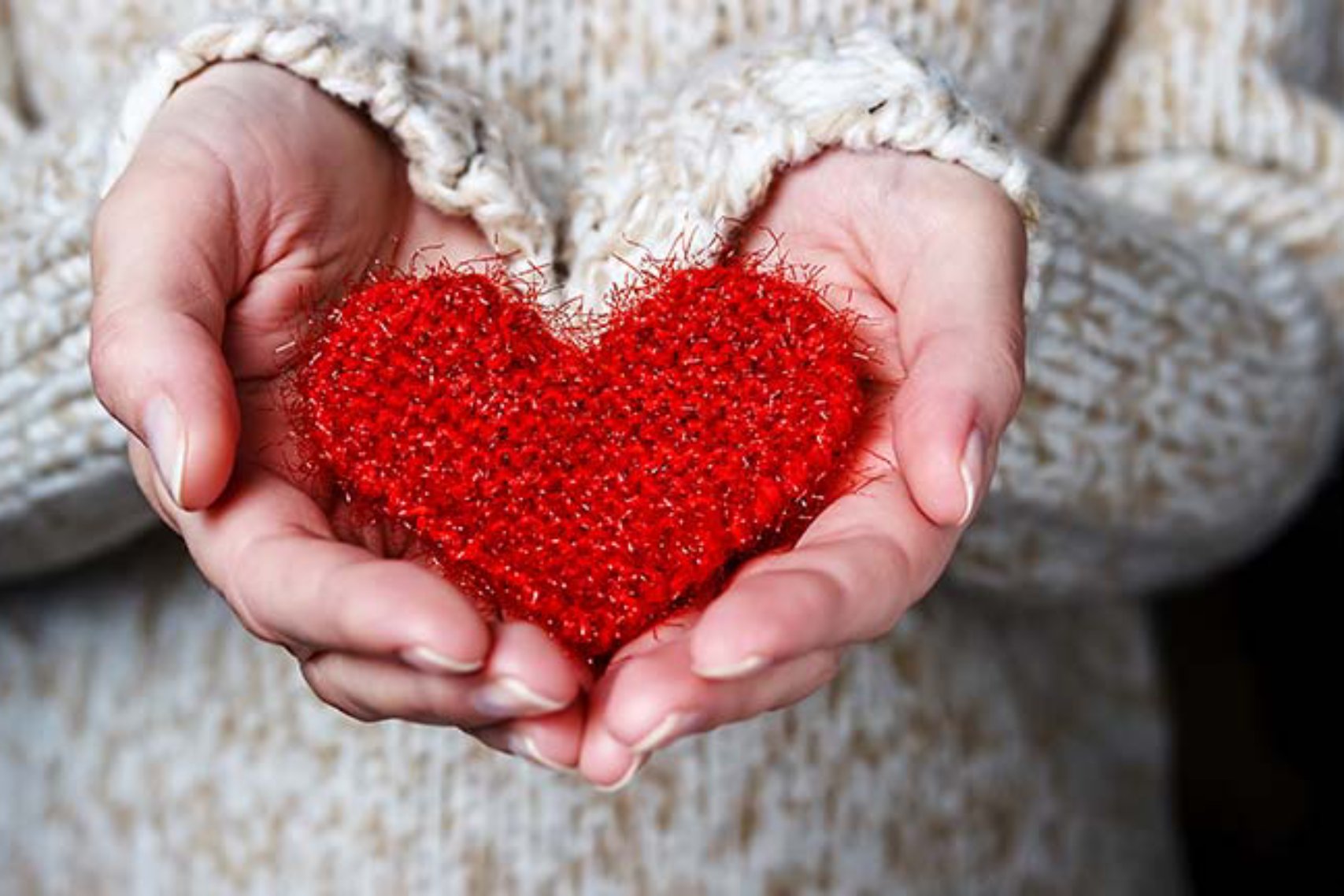 Heart shape held by the hands of someone wearing sweater