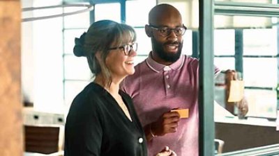 Photograph of a man and woman looking at a sticky note on a glass board.