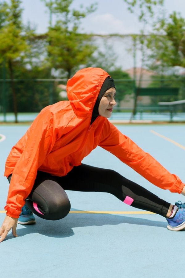 Sporty runner with hijab stretching legs in the park