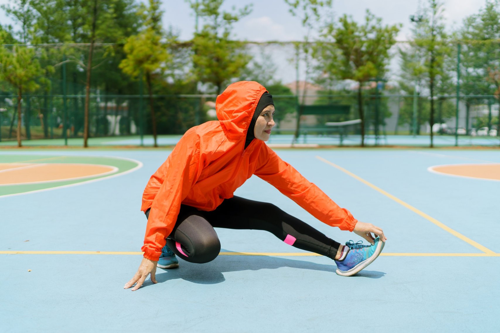 Sporty runner with hijab stretching legs in the park