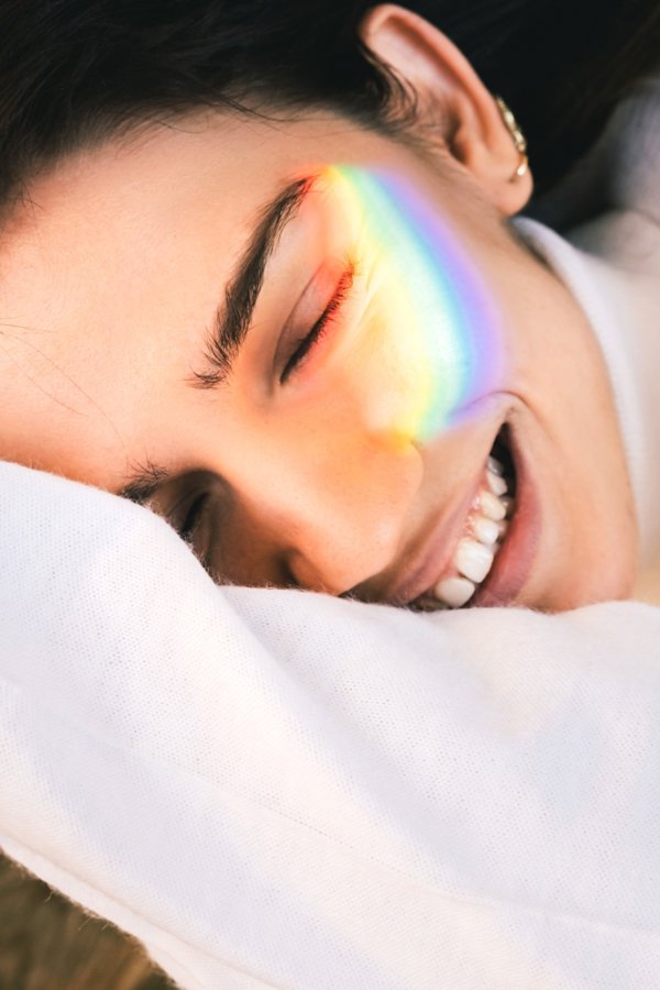 A beautiful young carefree woman smiling happily with her eyes closed, enjoying life, a rainbow sunbeam on her cheek. Concepts of happy relationships, the beauty of pride, uniqueness and diversity inclusion in modern society.